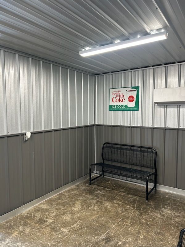 Small metal-walled room with fluorescent lights, a bench, and a sign on the back wall.