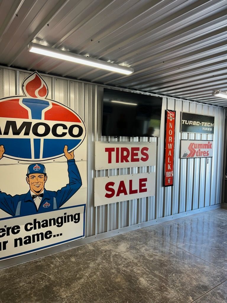Interior of a tire shop with a large “TIRES SALE” sign and automotive service banners on corrugated metal walls