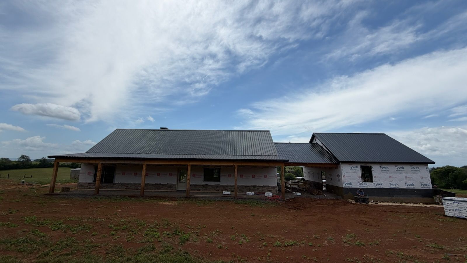 Rural house with metal roofs on a red dirt lot under a cloudy sky.