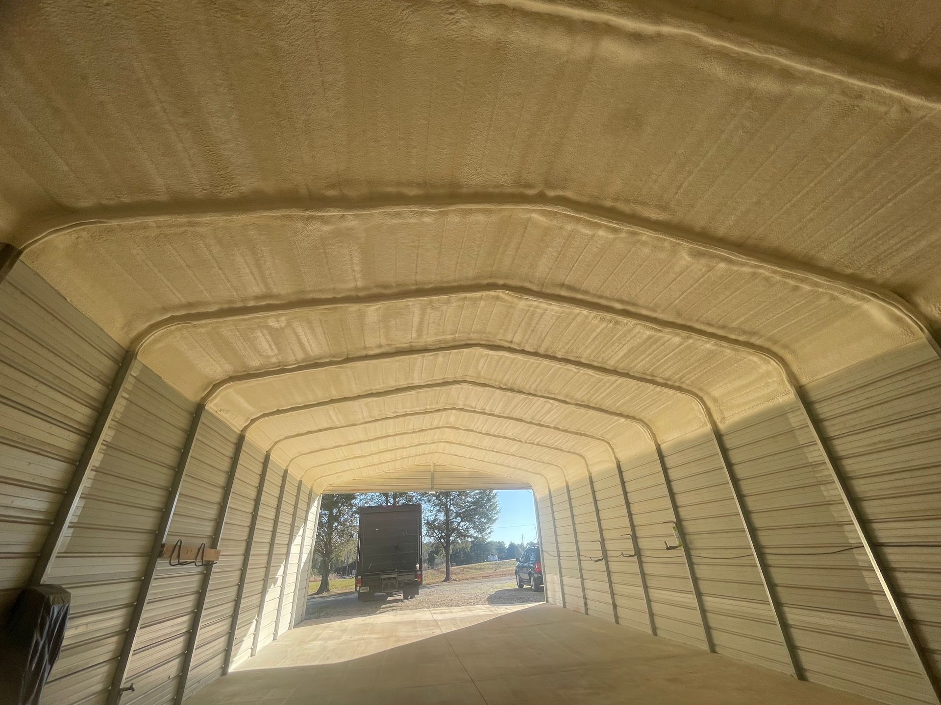 Interior of a metal building with spray foam insulation on the ceiling; view looking out towards a truck.