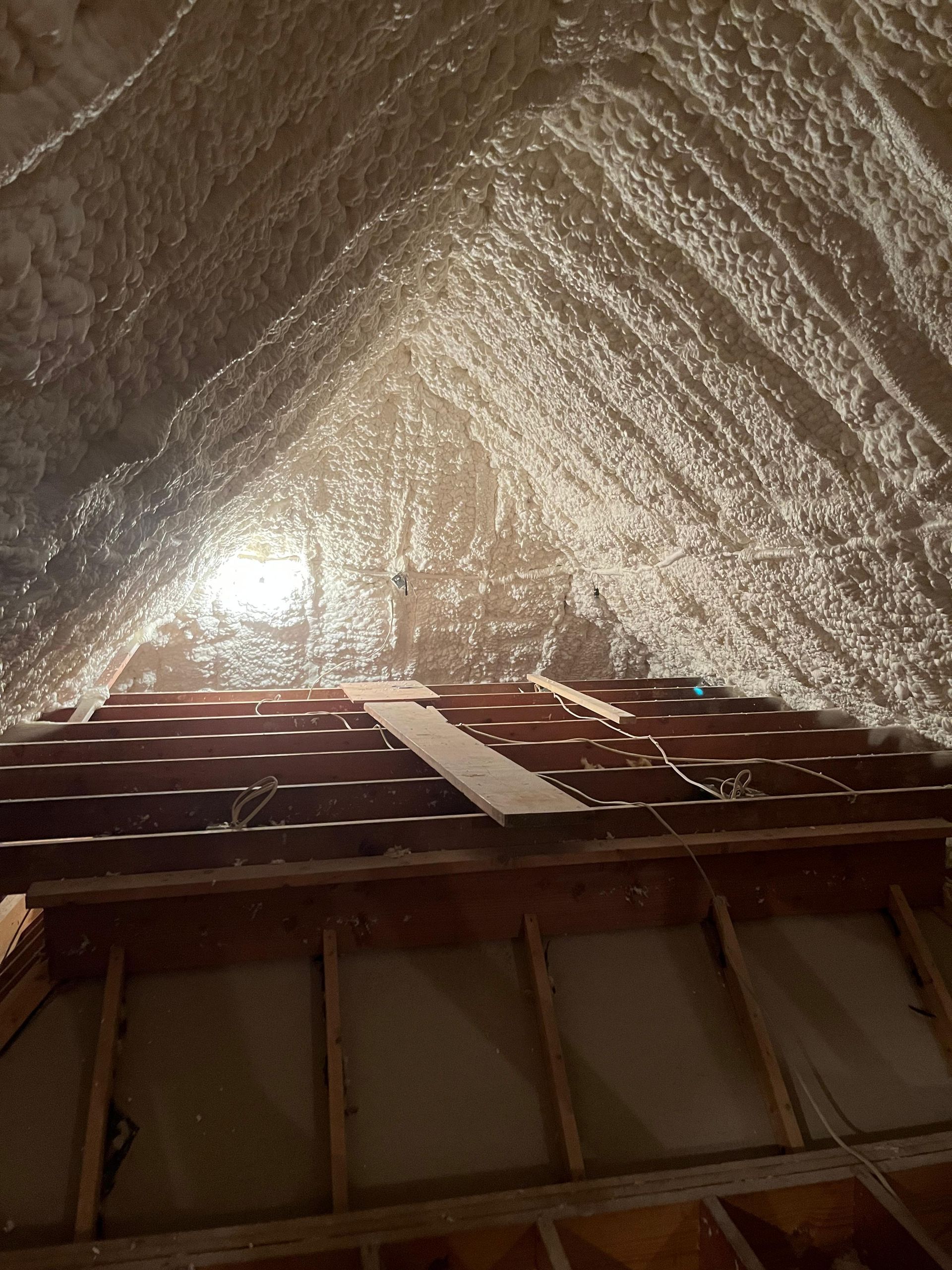 Attic interior with spray foam insulation. Wooden beams and boards are visible below the insulated roof.