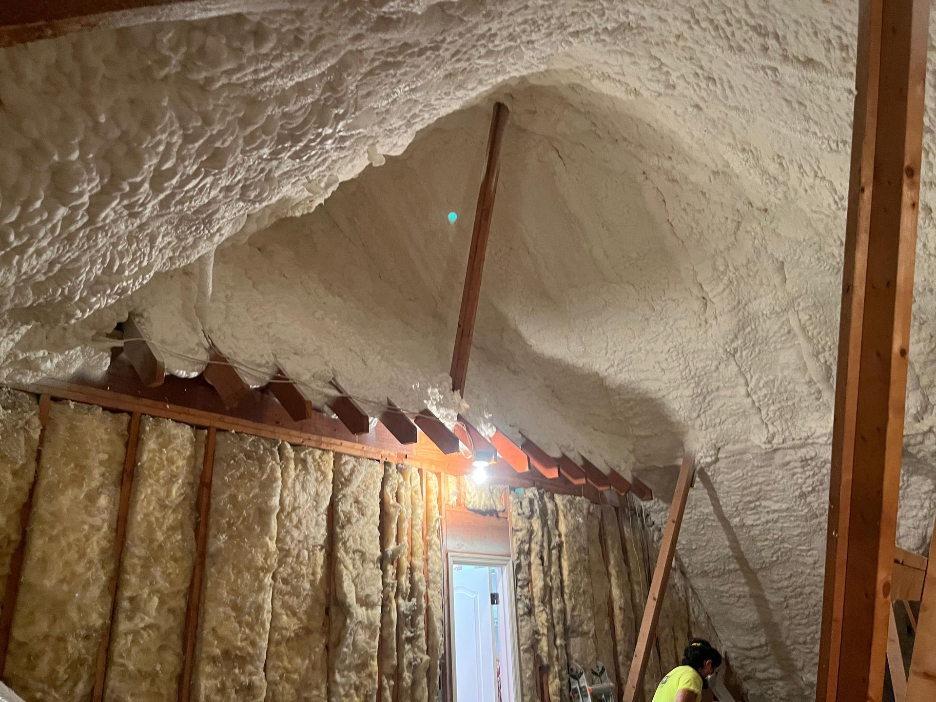 Attic with spray foam insulation on ceiling; fiberglass insulation on walls. A person works in the corner.
