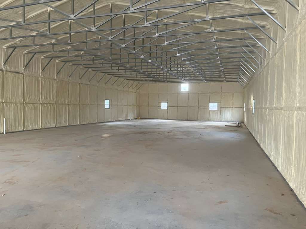 Interior of a large, empty warehouse with spray foam insulation on the walls and ceiling.