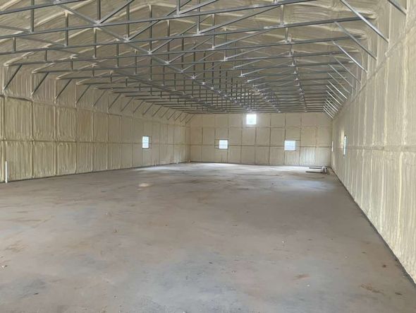 Interior of a large, empty warehouse with spray foam insulation on the walls and ceiling.