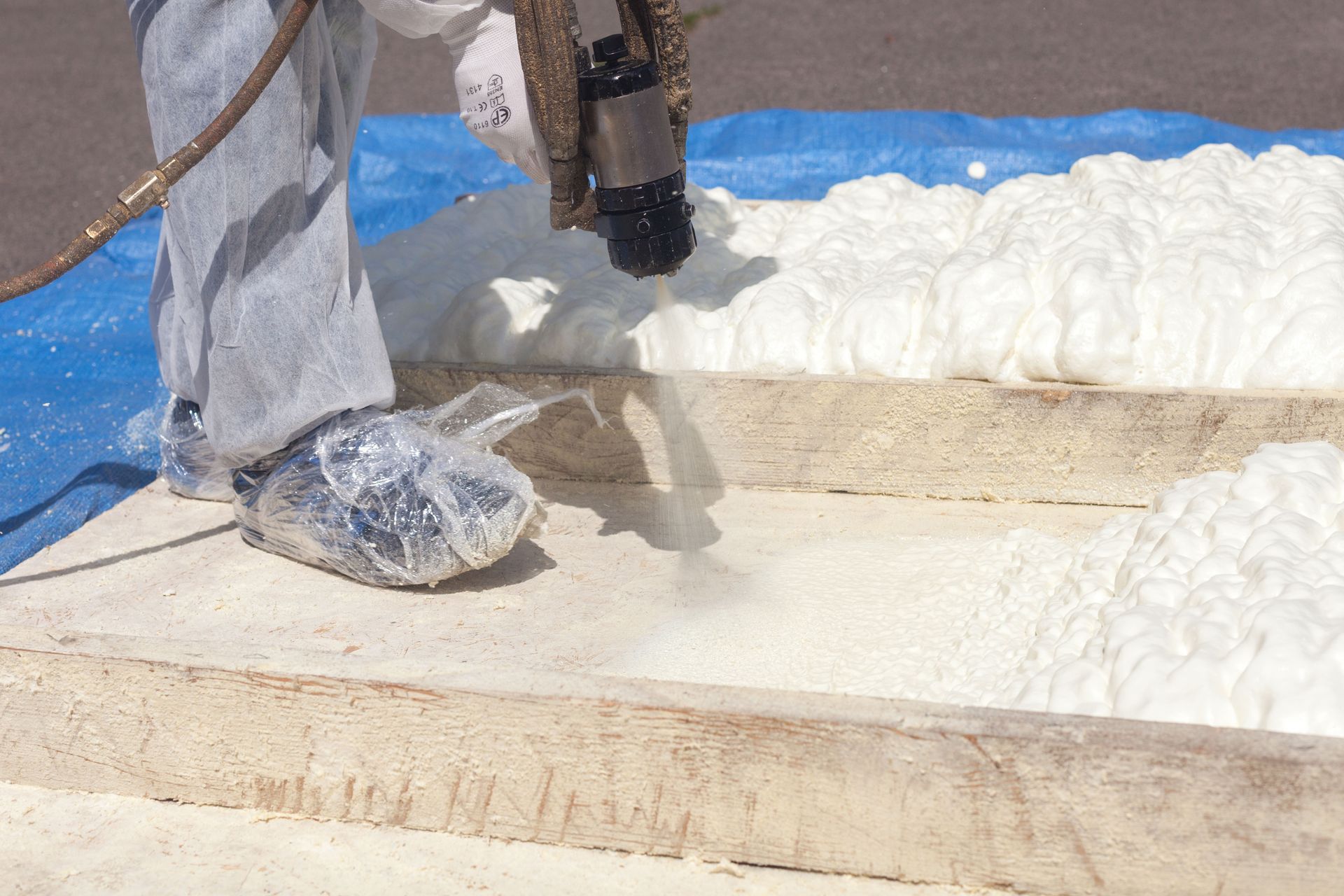 Person spraying expanding foam insulation into a wooden frame.