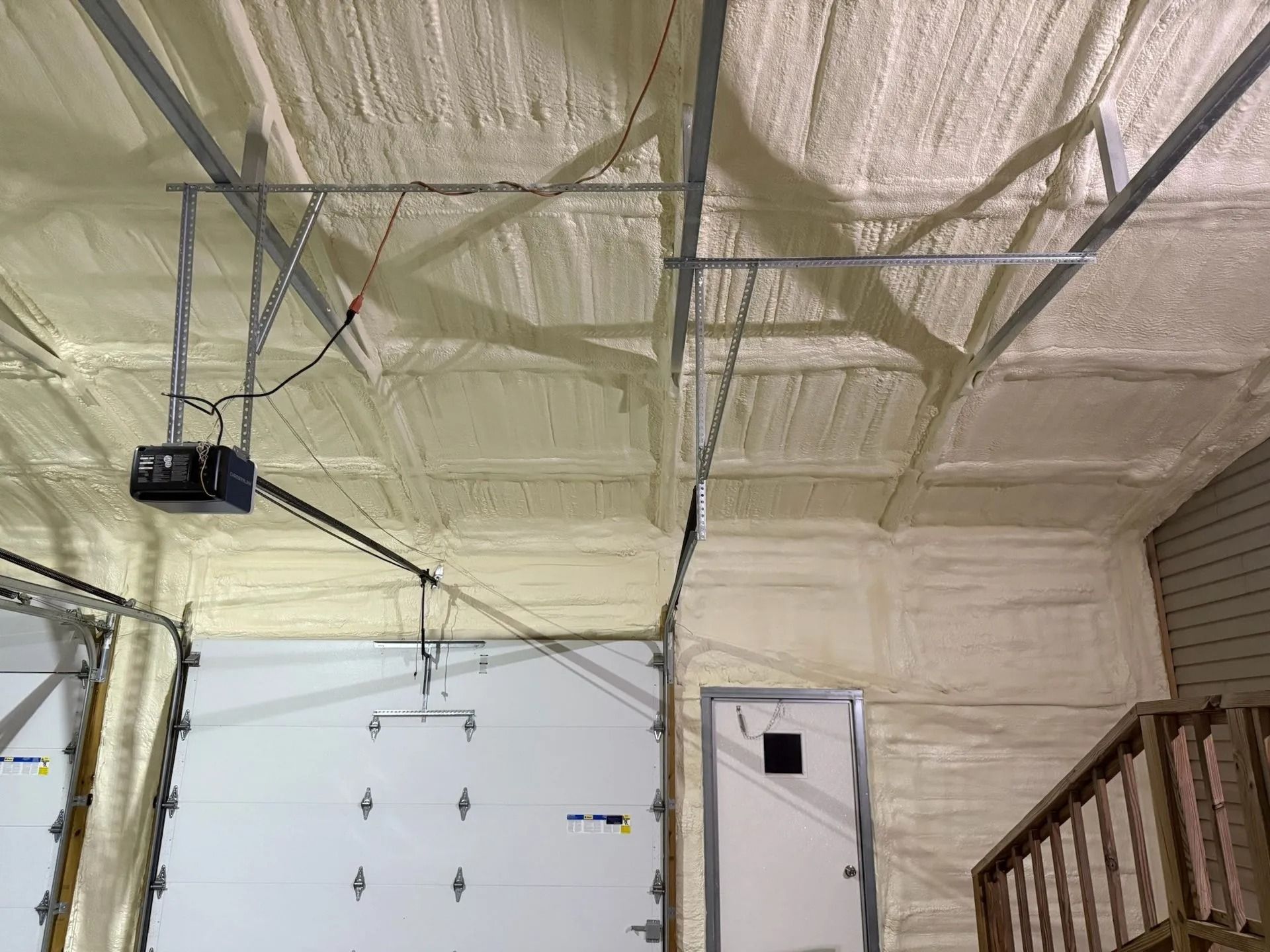 Garage interior with spray foam insulation on ceiling and walls. Garage doors and a white door are visible.