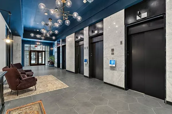 Lobby with three elevators, seating area, and patterned rug. Blue ceiling, marble walls, and dark gray flooring.