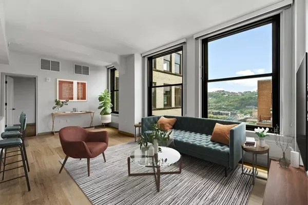 Living room with a blue sofa, brown armchair, large windows, and cityscape view.