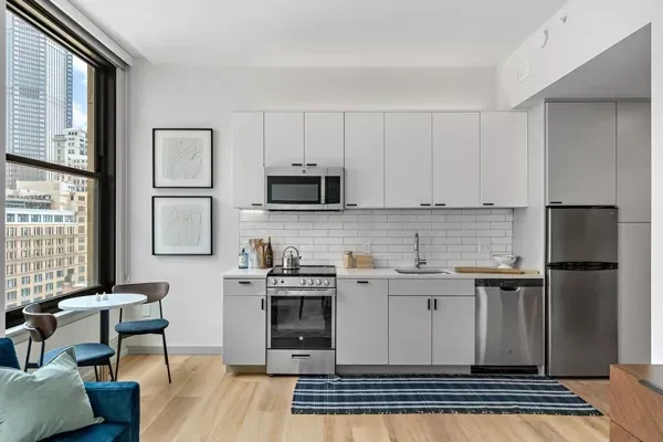 Modern studio kitchen with white cabinets, stainless steel appliances, and a city view.