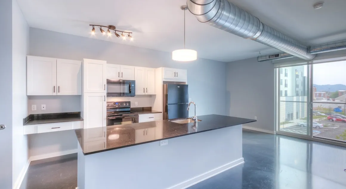 Modern kitchen with white cabinets, black appliances, and dark countertop island. Large window with a view.
