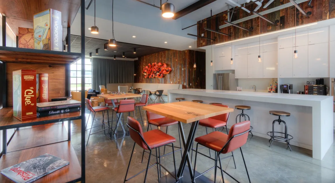 Modern, open-plan office lounge with wooden shelves, red chairs, and a white kitchen.