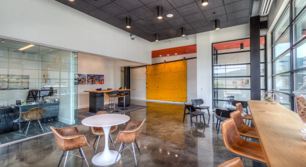 Modern office interior with glass walls, yellow accent wall, and round white table with chairs.