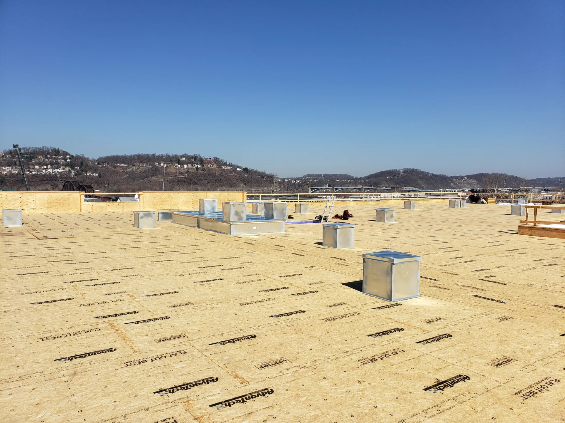 Flat rooftop under construction with ventilation units and a view of distant hills.