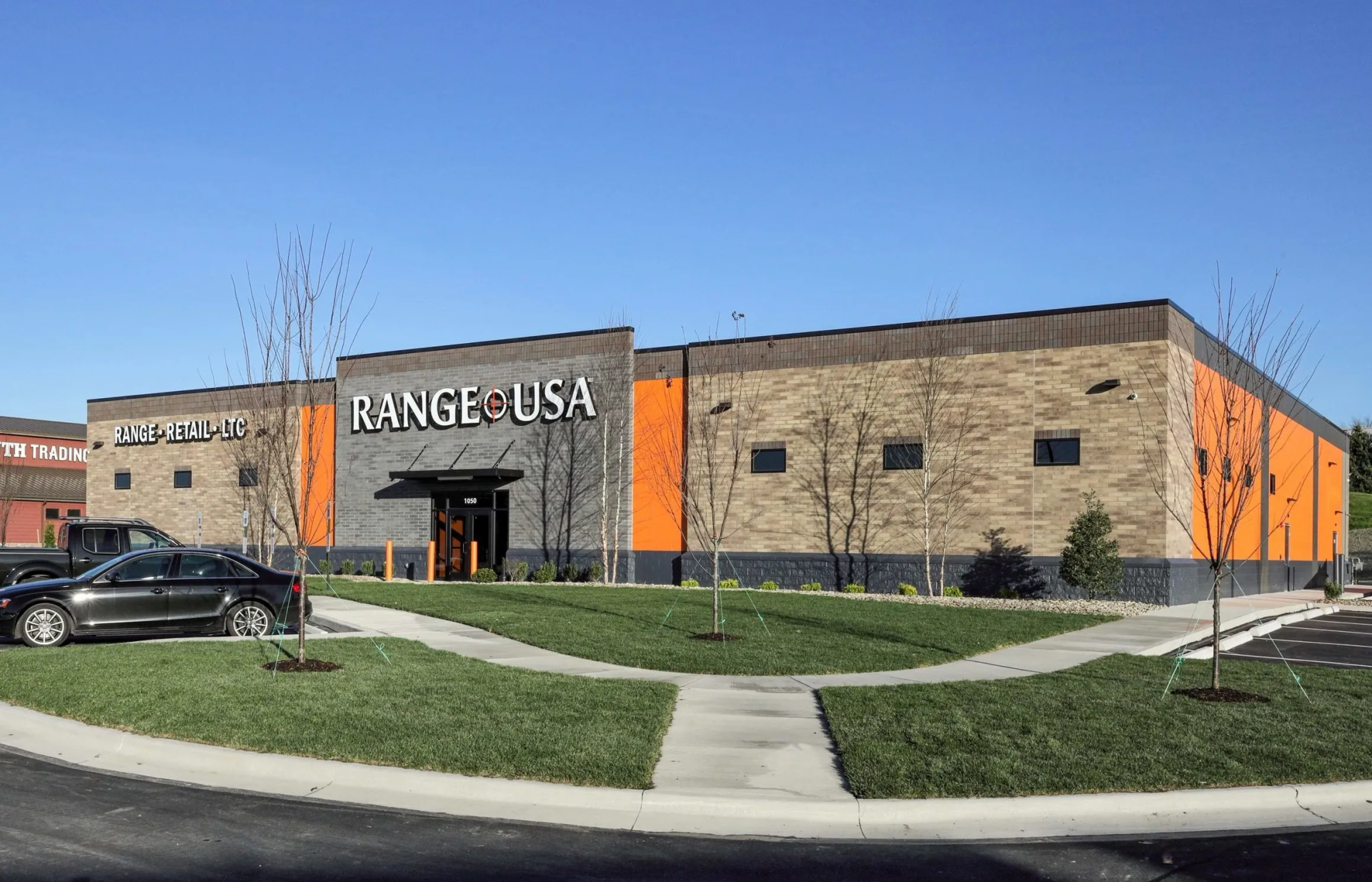 Exterior of Range USA building with signage. Orange accents, brick and black detailing, blue sky.