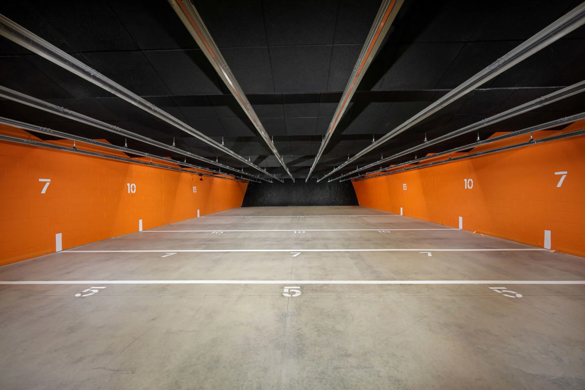 Interior of a shooting range, with orange walls, numbered firing lanes, and a black ceiling.