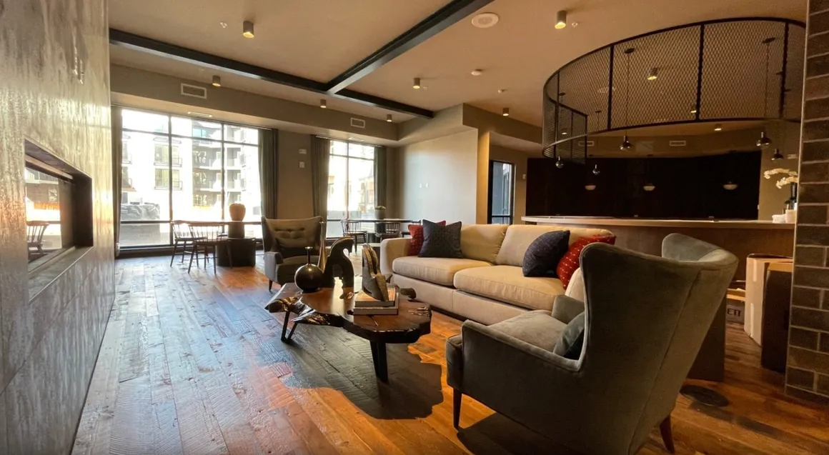 Upscale lounge with a fireplace, comfortable seating, large windows, and a modern light fixture.