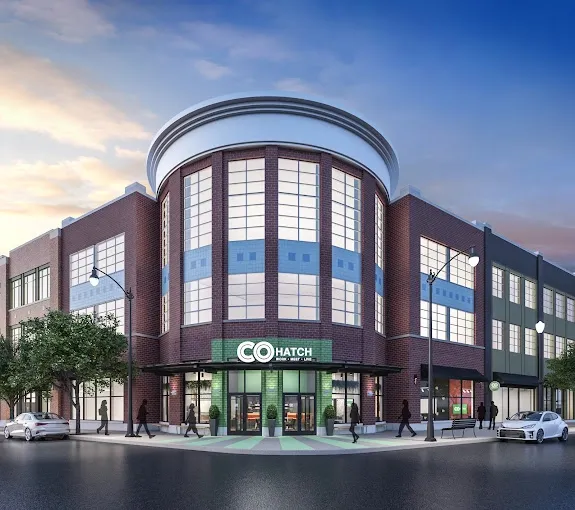 Modern brick commercial building with large windows and a circular top. People walk on the sidewalk.