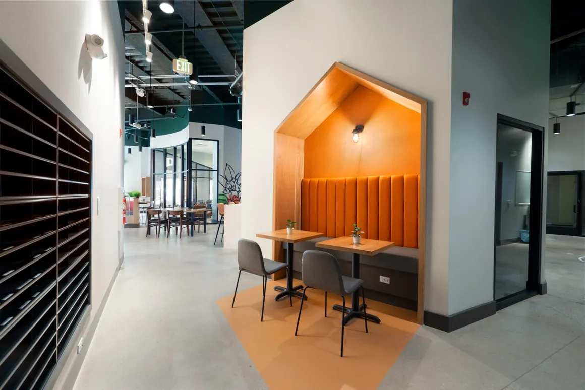 Interior hallway with seating nook and tables; orange and gray accents.