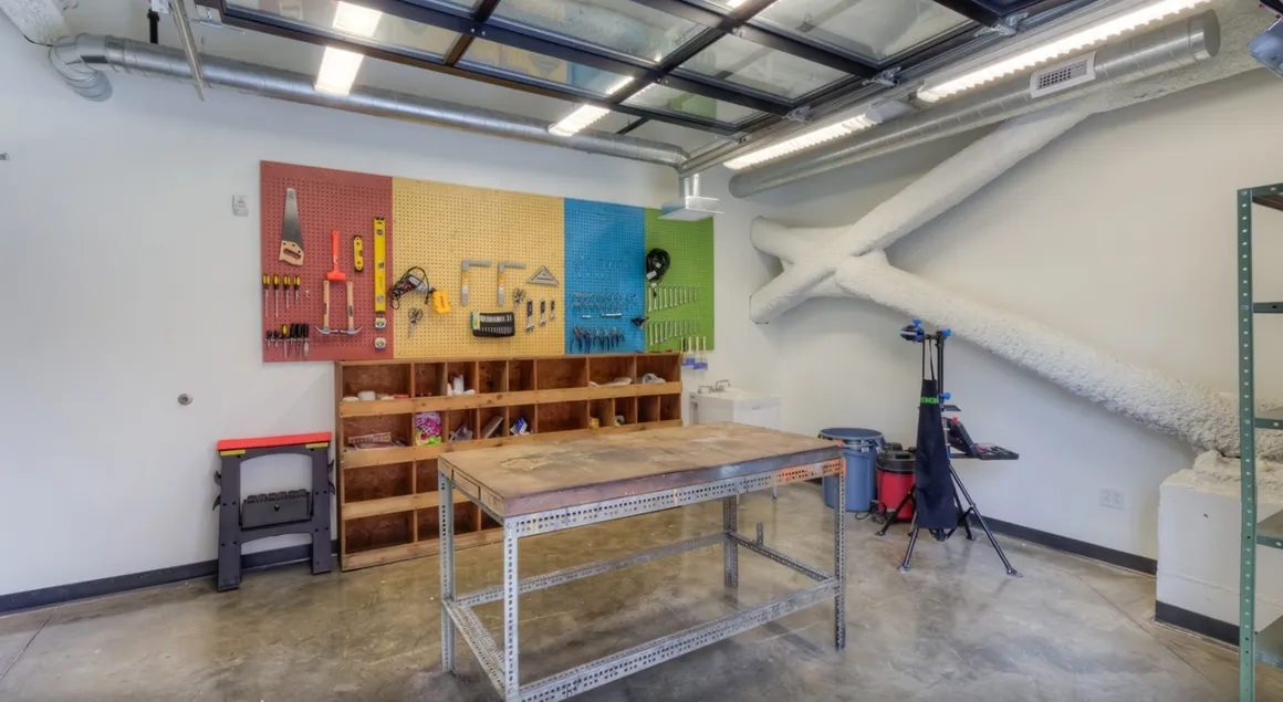 Workshop with colorful pegboard, tools, workbench, storage shelves, and white walls.