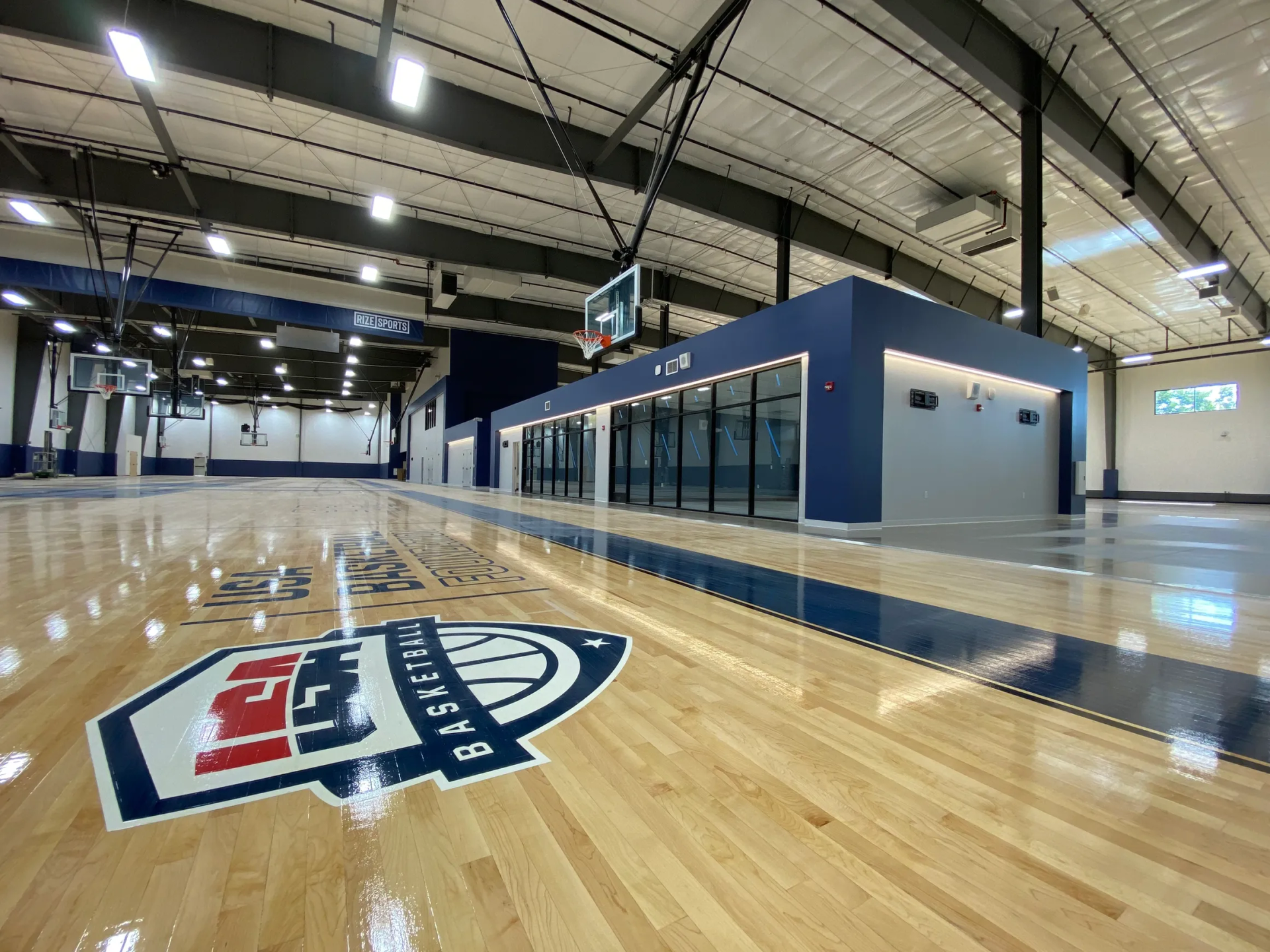 Basketball court with logo on floor, blue and white accents, indoor setting.