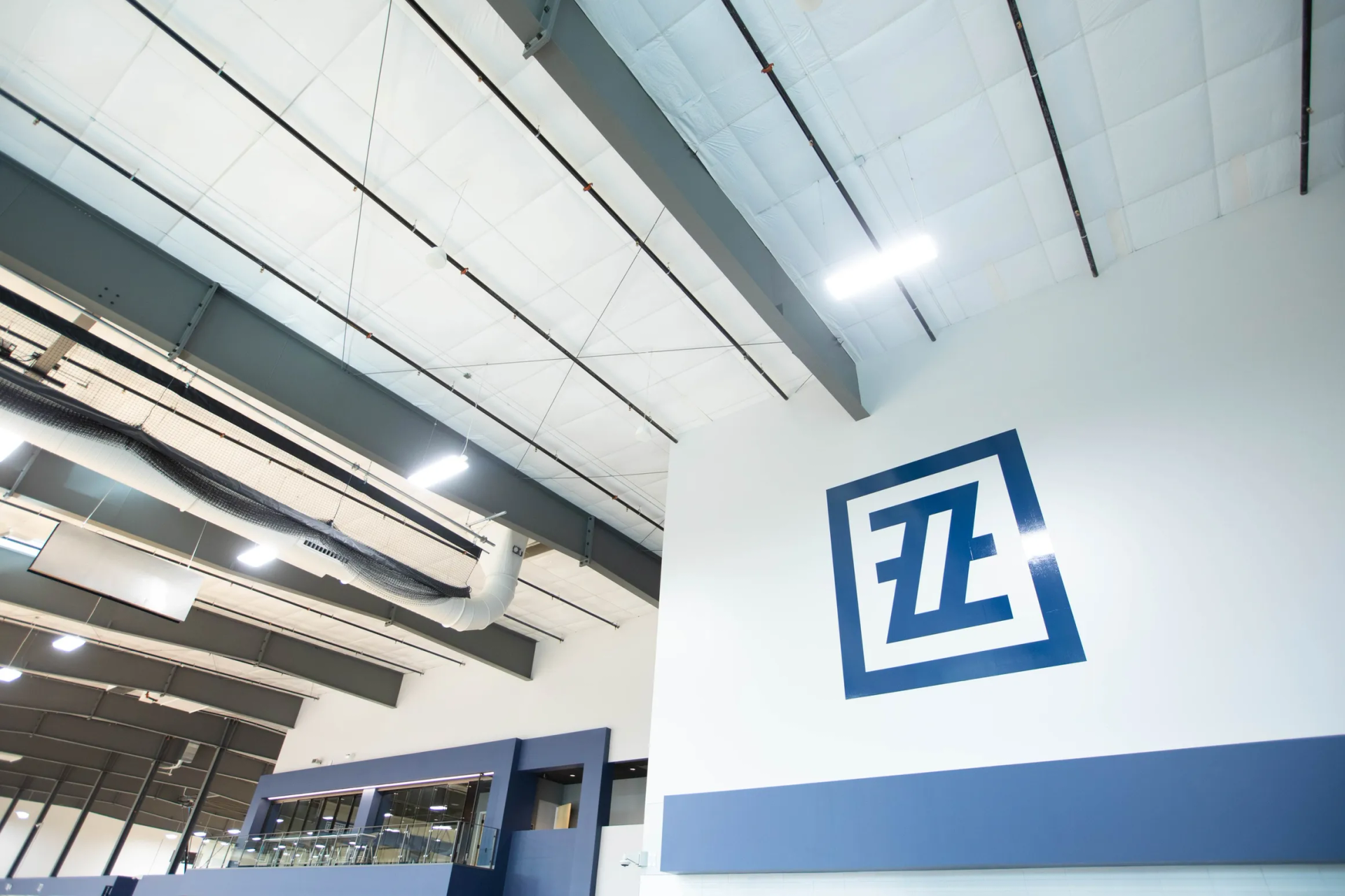 Blue logo with an E and a Z on a white wall. The room has a high ceiling and metal beams.