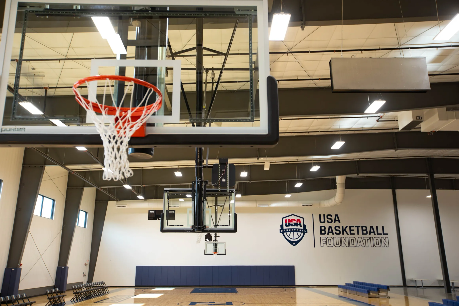 Basketball court with hoops; USA Basketball logo on wall, empty, indoor setting.
