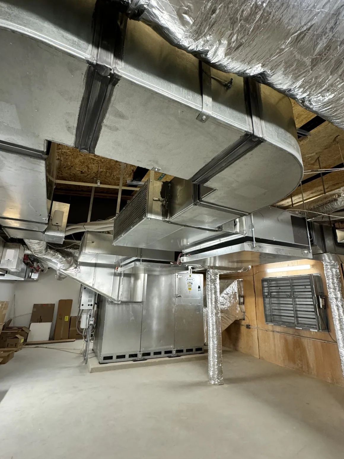 HVAC ductwork in a construction setting, featuring metal rectangular ducts overhead, with unfinished walls and flooring visible.