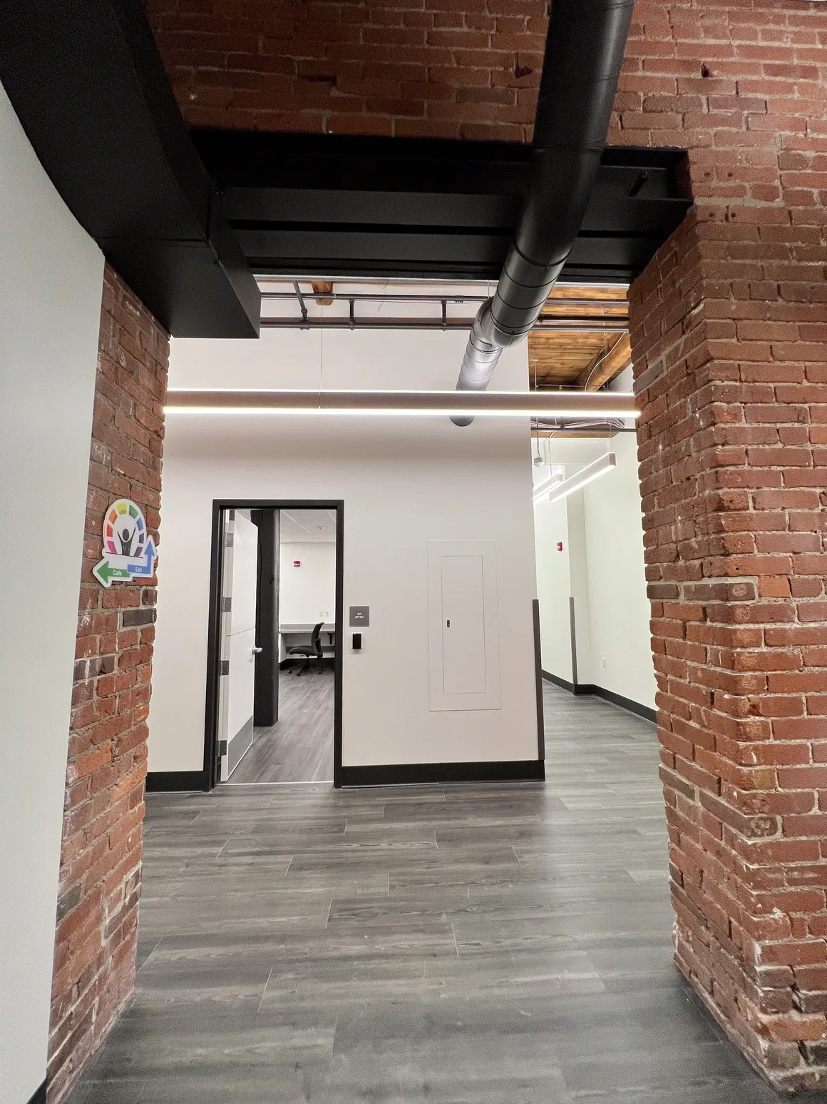 Interior hallway with exposed brick columns, black ceiling beams, and a view into a room with a closed door.