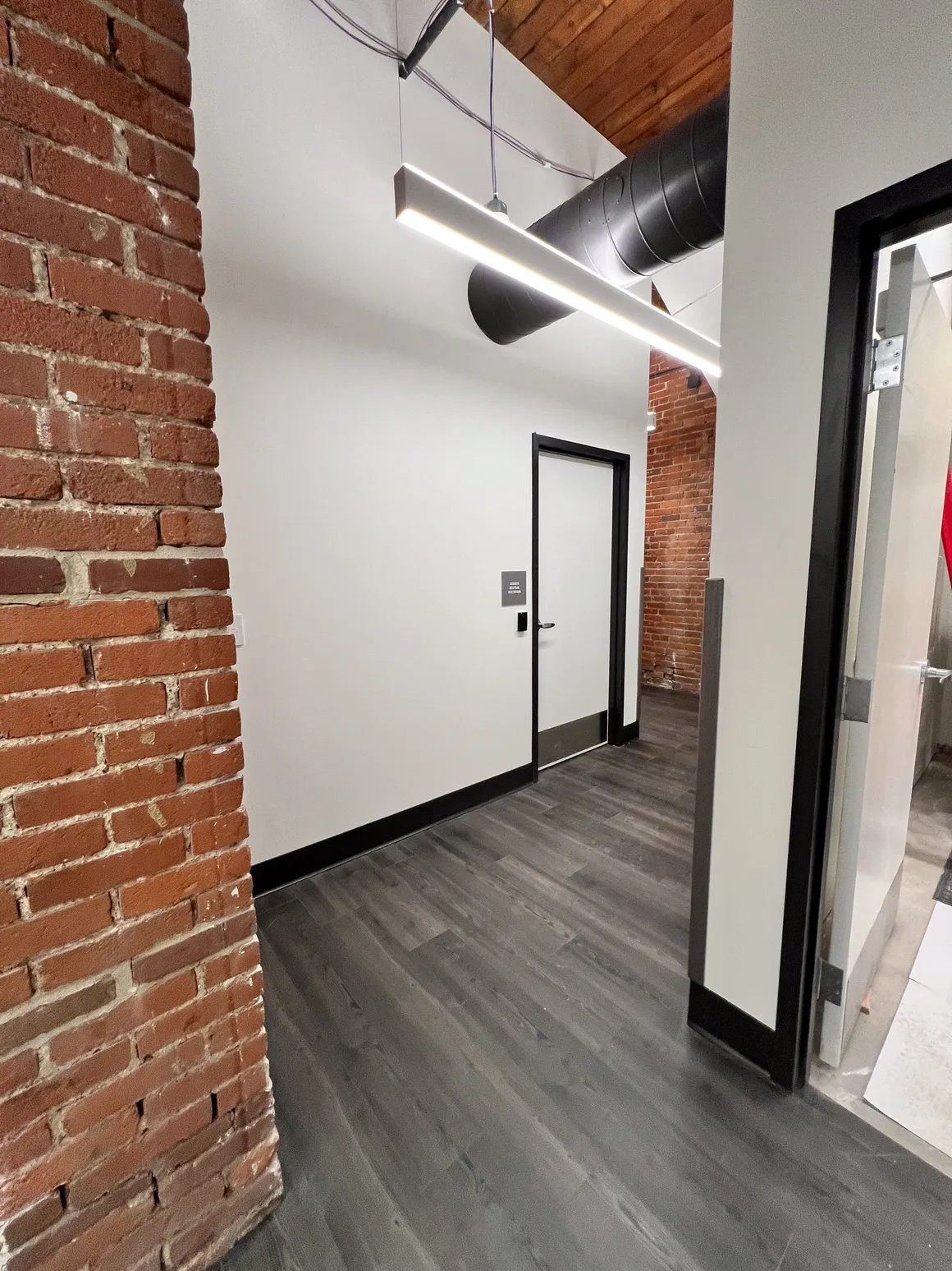 Hallway with brick wall, white walls, dark trim and gray flooring.