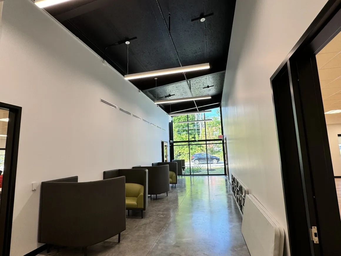 Hallway with seating, white walls, black ceiling, glass door at the end.