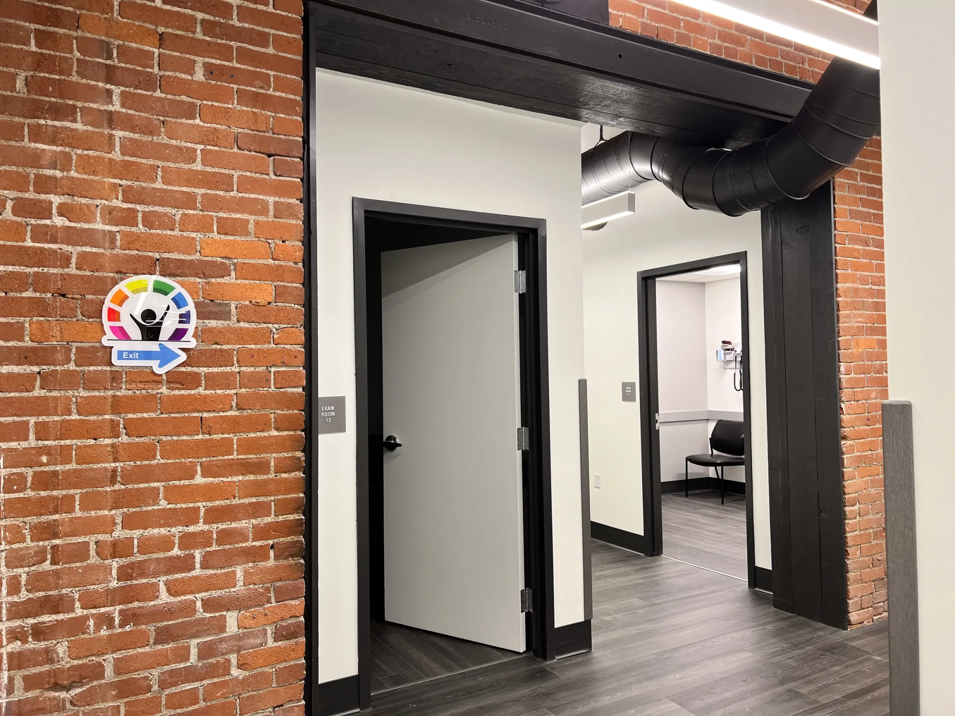 Hallway with red brick wall, white doors, and a sign for Lift with a rainbow logo.