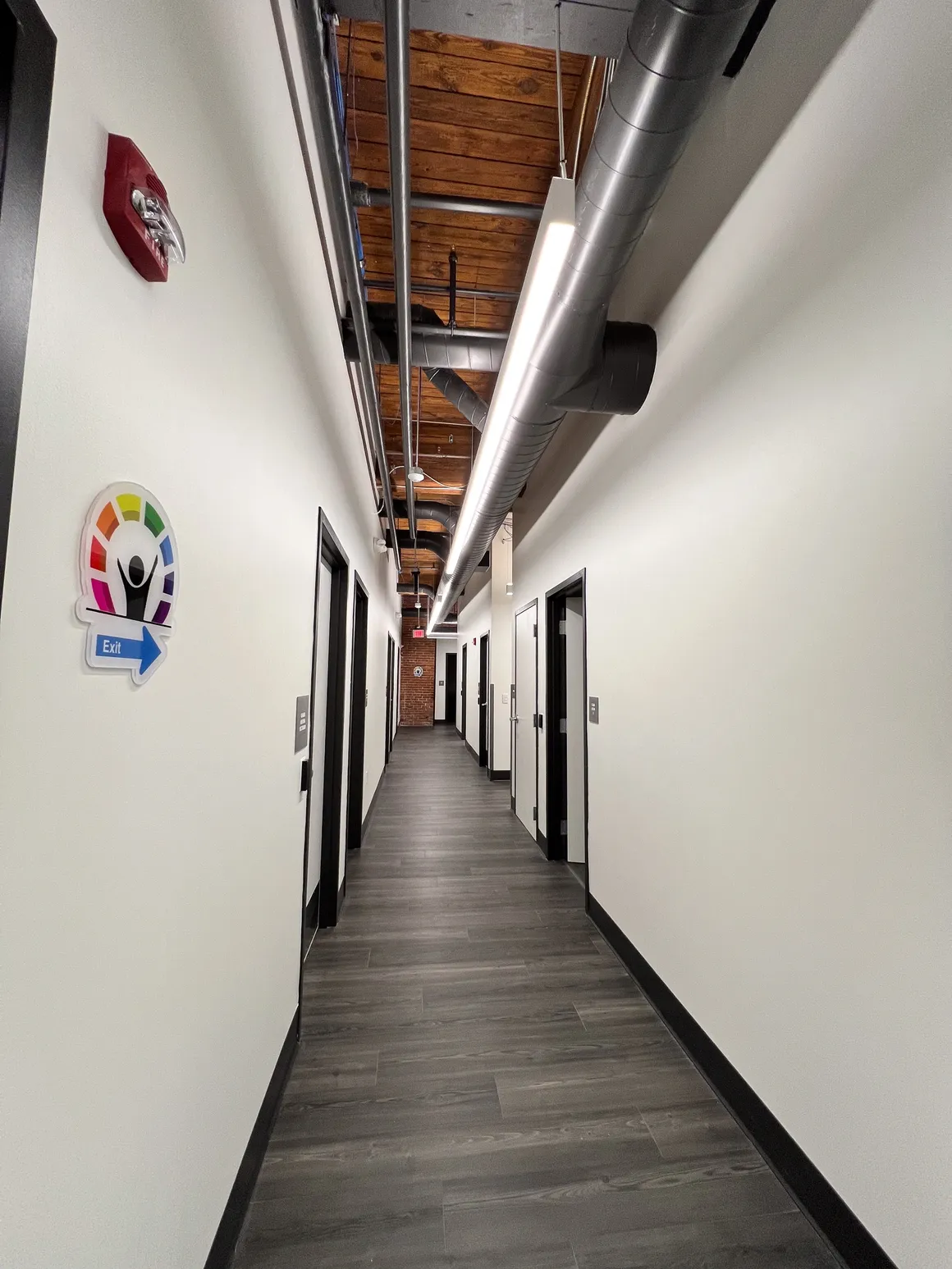 Long hallway with dark doors, a wooden ceiling, and white walls.