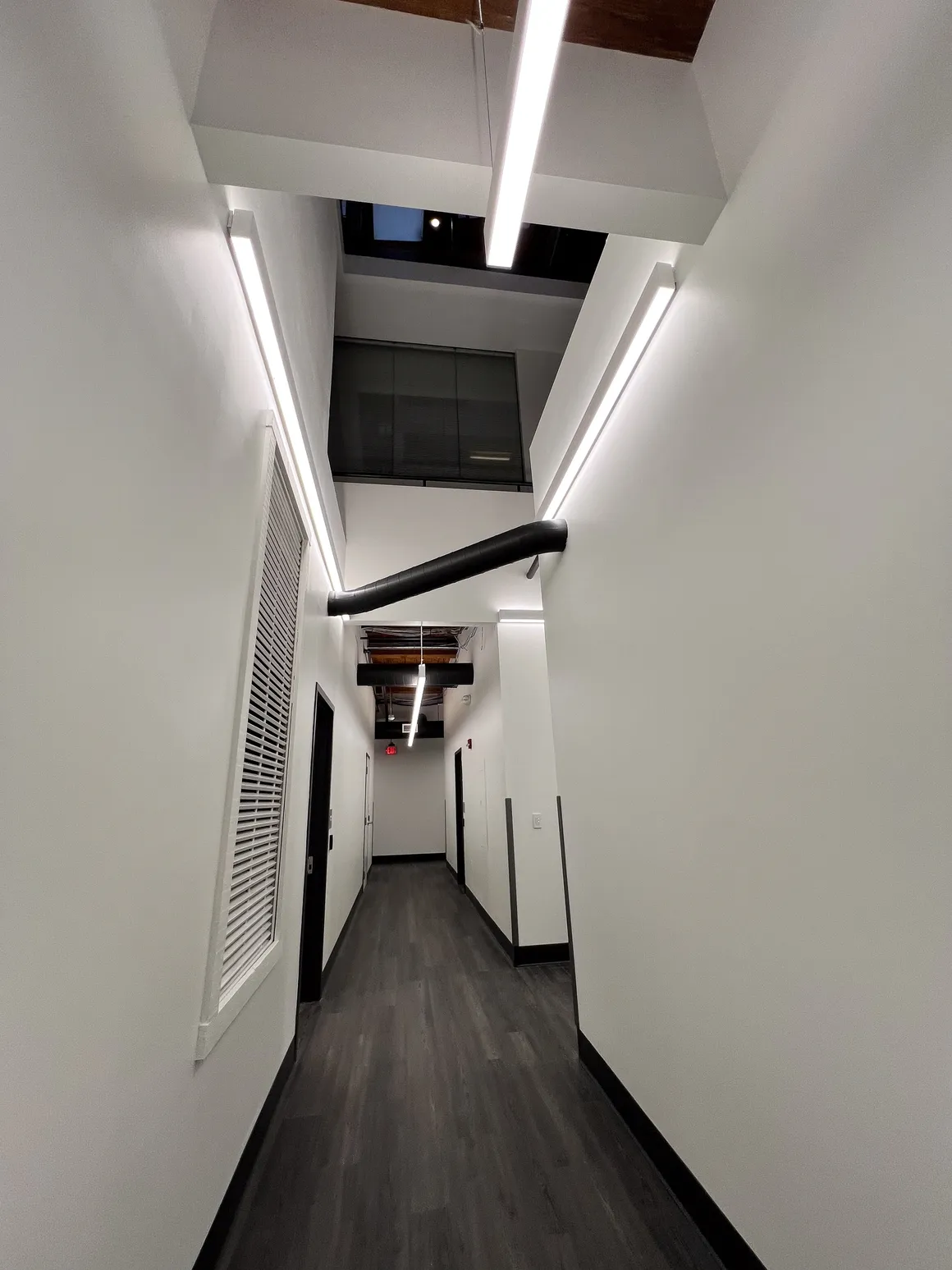 Narrow hallway with white walls, dark floor, and bright overhead lights.