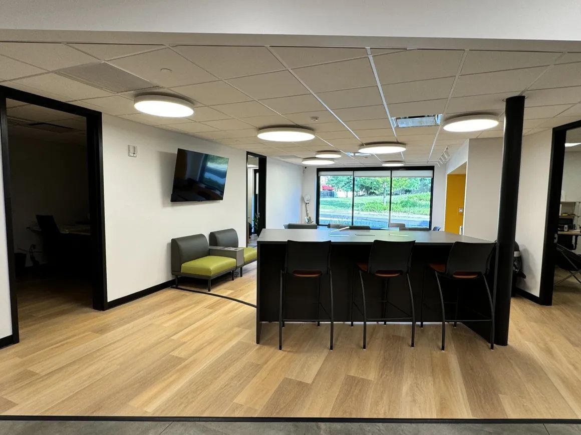 Modern office break room with bar seating, couches, a TV, and large windows.