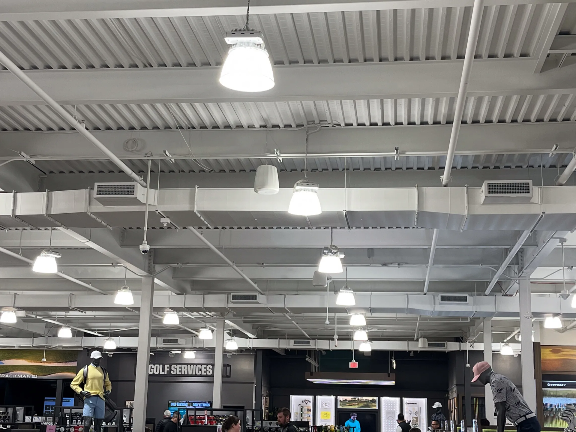 Interior view of a golf shop with overhead lighting, ductwork, and mannequins displaying clothing.