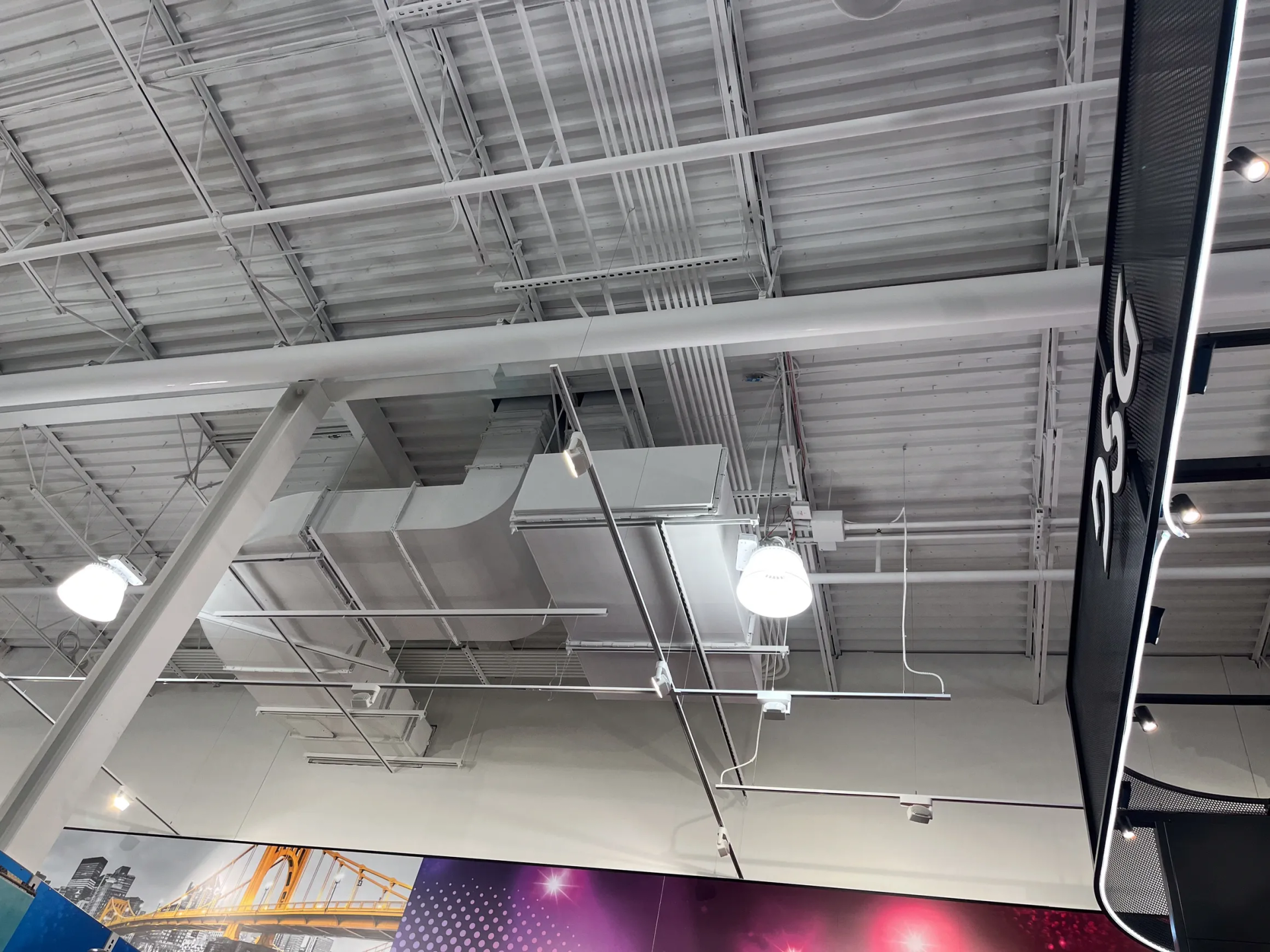 Overhead view of a white commercial ceiling with ductwork, pipes, and lighting.