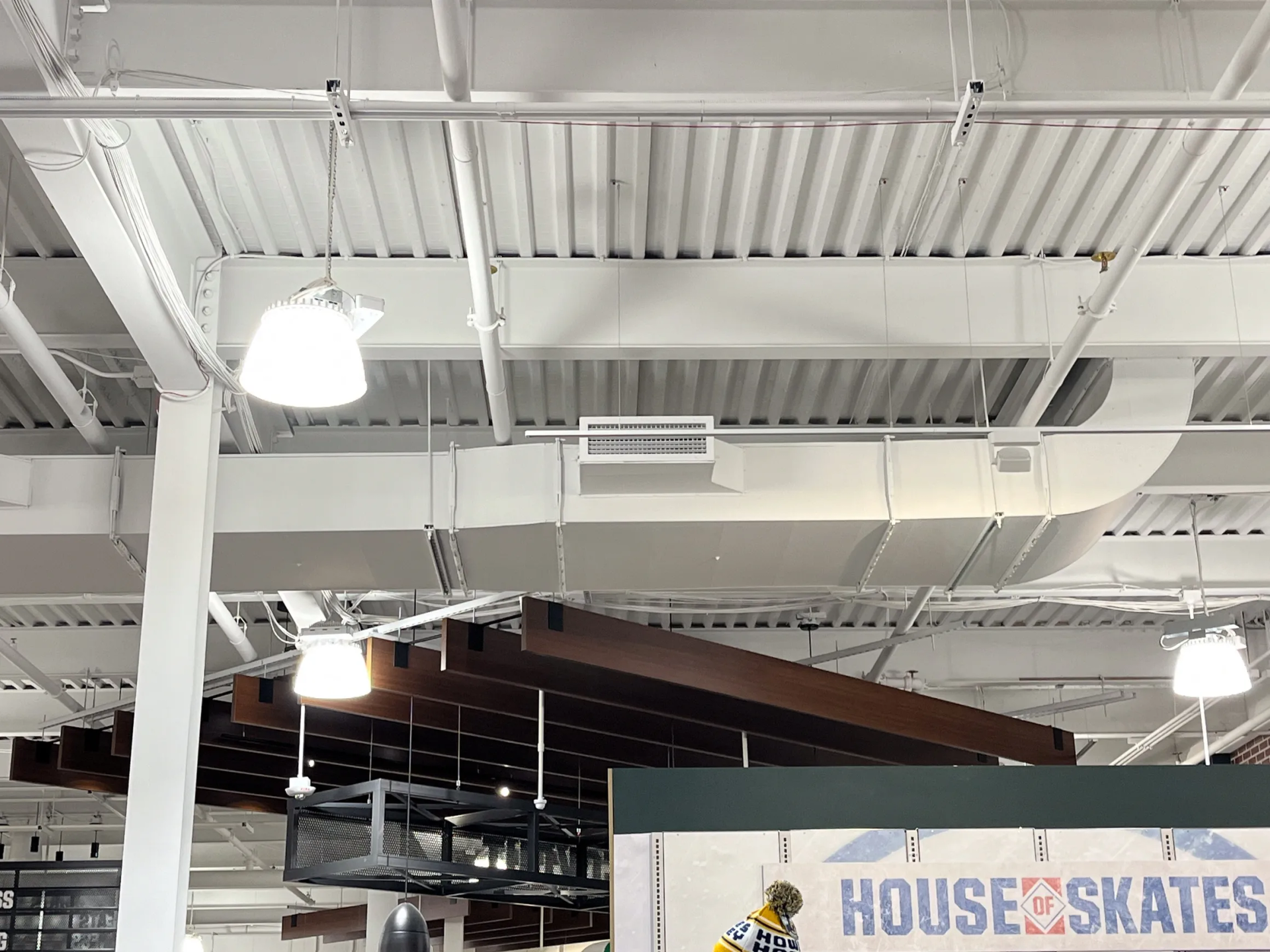 White ceiling with exposed beams, ductwork, and hanging light fixtures in a retail space.