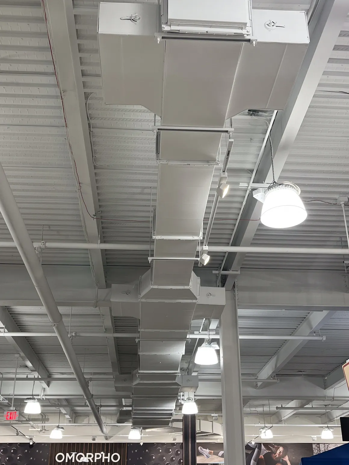 White ceiling with HVAC ductwork and hanging lights in a retail space.