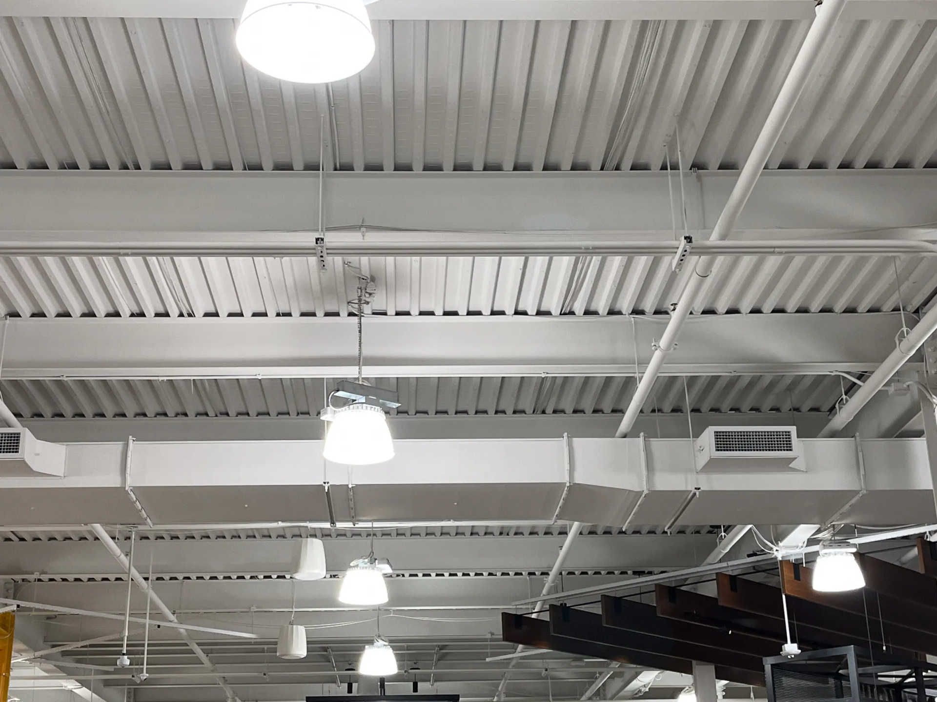 White ceiling with exposed beams, air ducts, and hanging lights.
