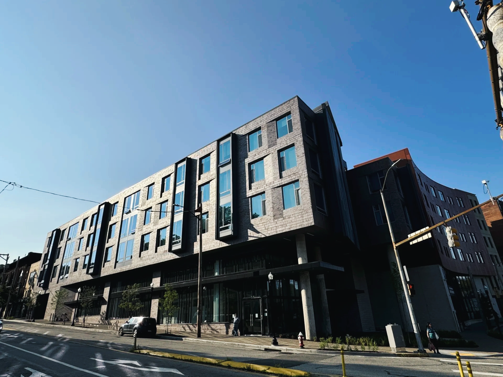 Modern multi-story building with dark facade, large windows, and street view under blue sky.