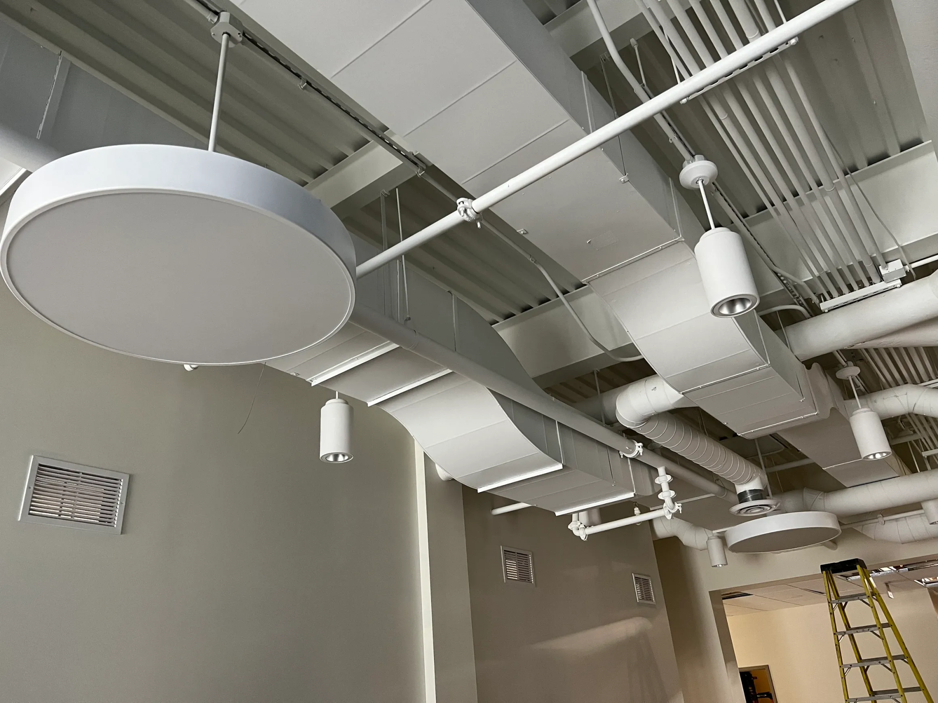 White ceiling with exposed ducts, pipes, and light fixtures. Walls are beige.