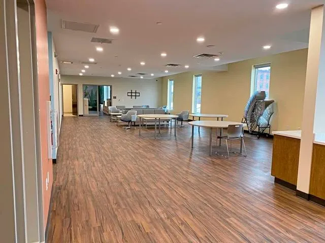 Spacious room with wood-look flooring, tables, chairs, and neutral-colored walls. Windows and doorways.