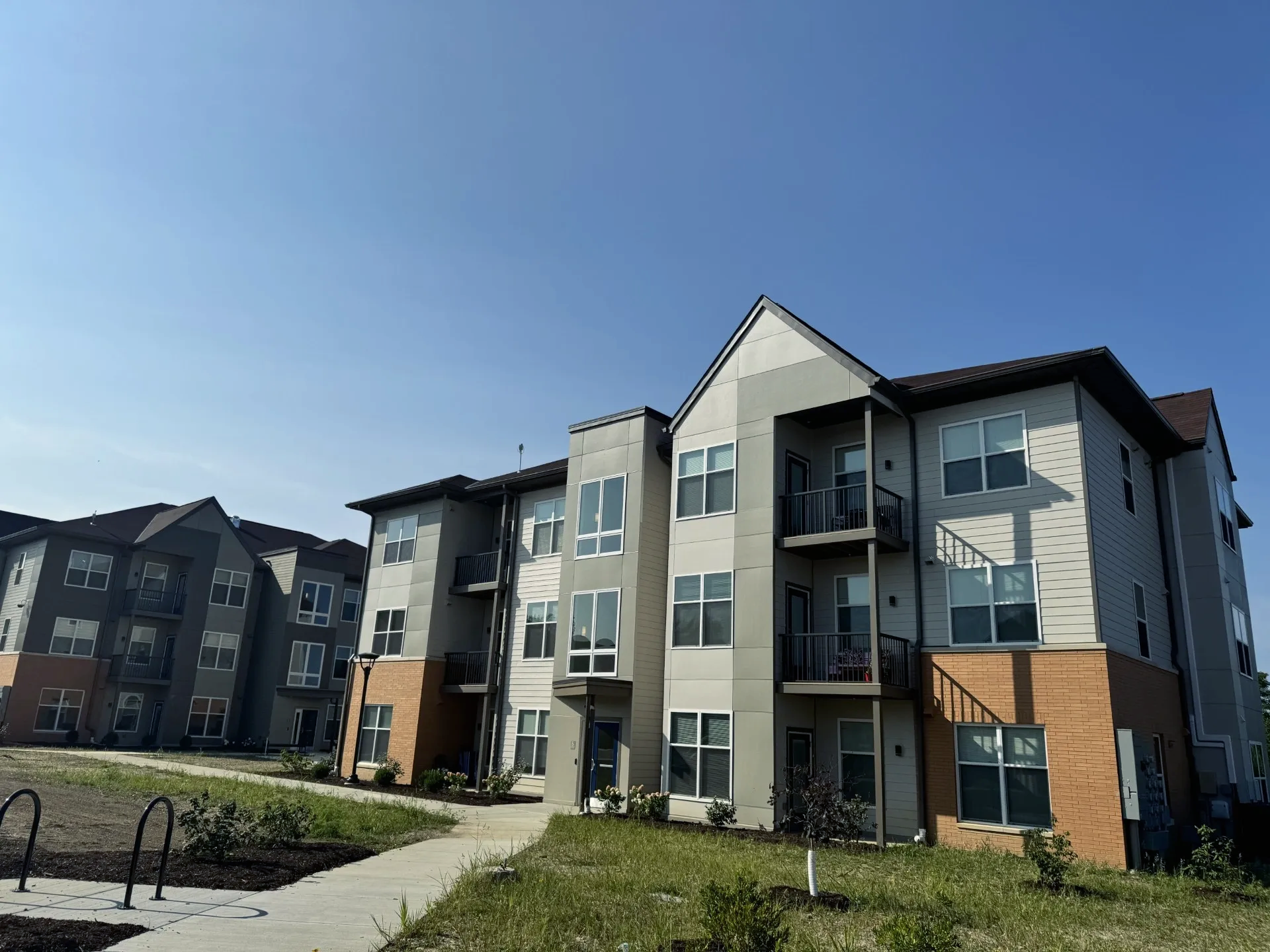 Apartment buildings with gray siding, red brick, and balconies against a blue sky.