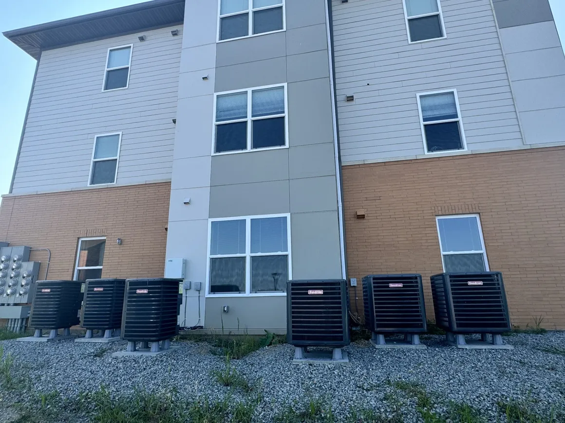 Air conditioning units lined up outside a multi-story building with windows.