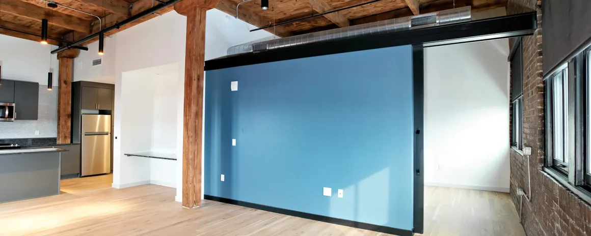 Modern industrial-style interior. Open-plan living space with exposed beams, brick wall, and large blue sliding door.