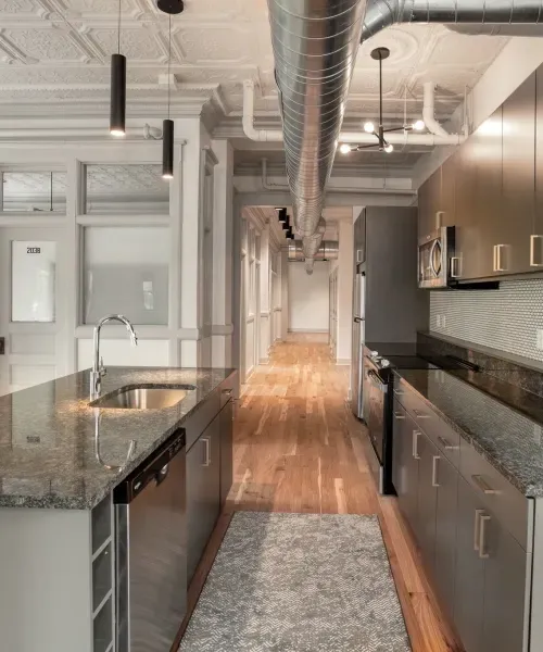 Modern kitchen with stainless steel appliances, granite countertops, and exposed ductwork.