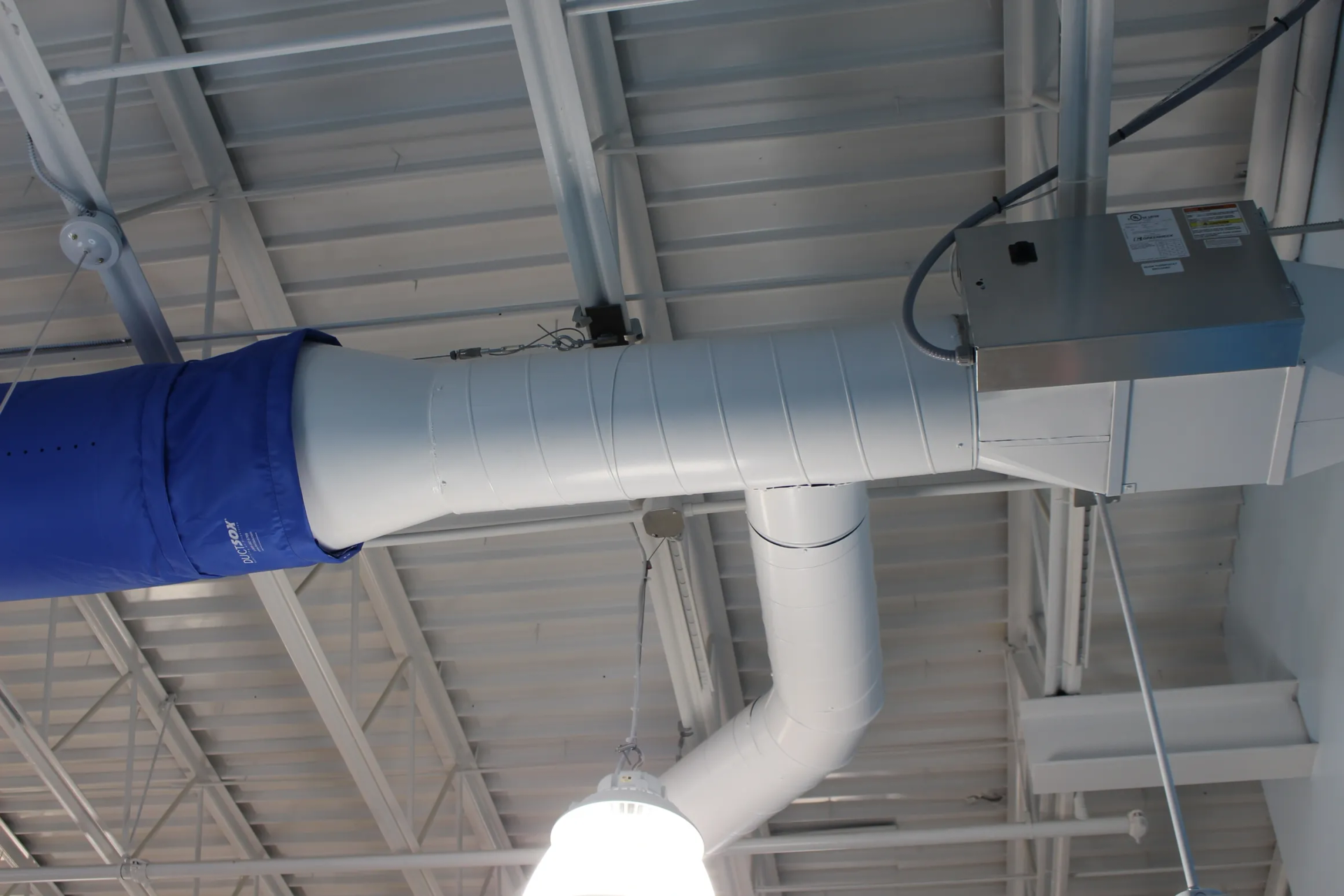 HVAC ductwork: white, cylindrical, and blue fabric sections run across a white ceiling in a commercial building.