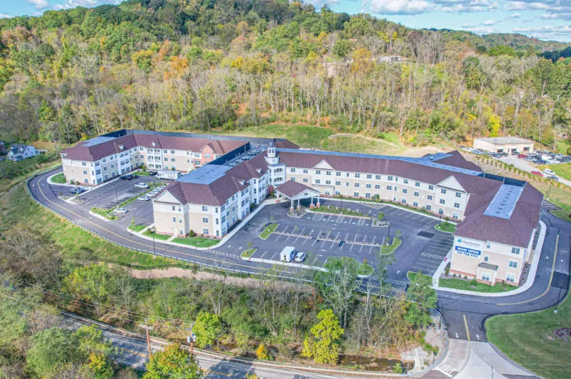 Aerial view of a multi-story building with a circular driveway and parking lot, surrounded by trees on a hillside.