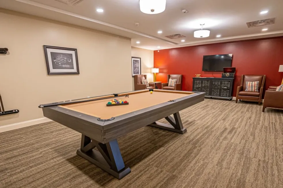 Pool table in a game room with red and tan walls, a TV, and chairs.