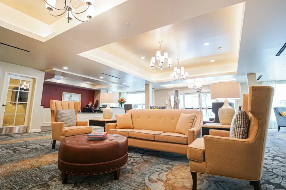 Lobby with seating: tan sofa, armchairs, and ottoman, neutral colors, chandeliers, and patterned carpet.